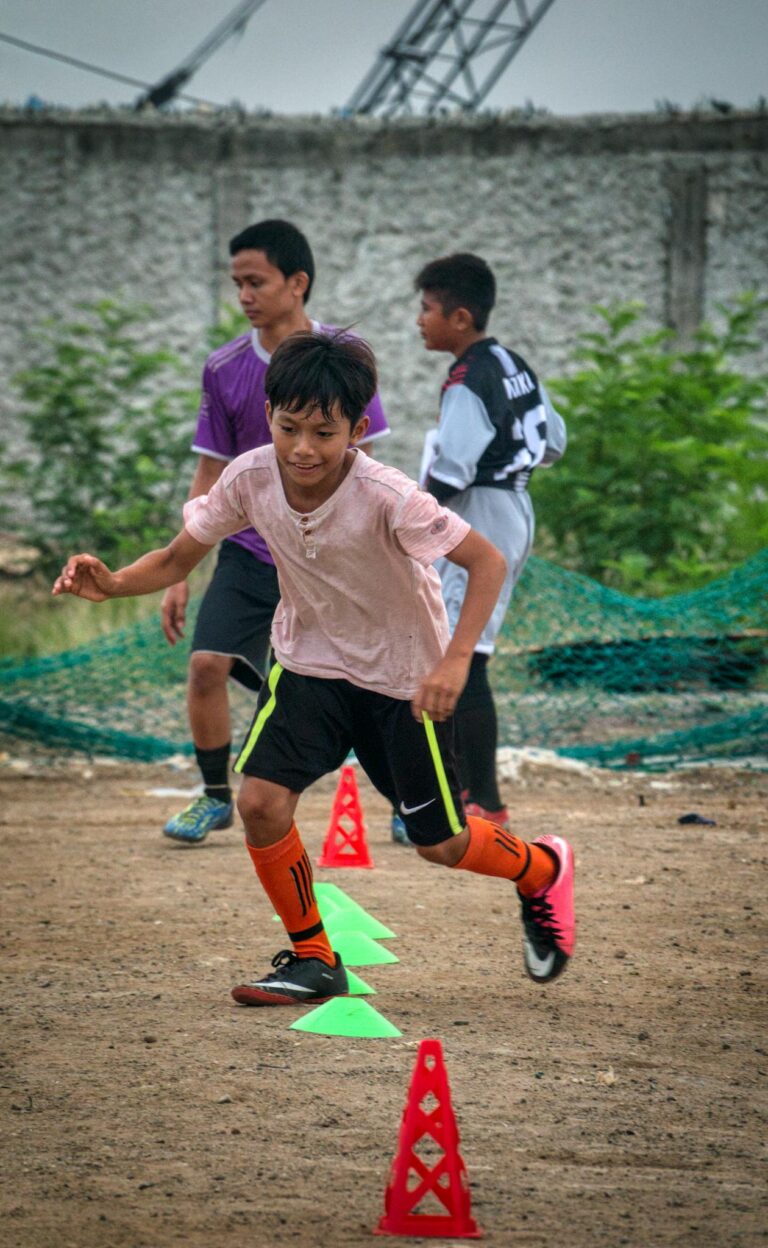 Ethnic kid running through training cones while playing football with team players on field